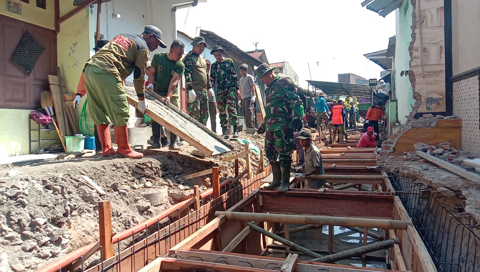 mbminvestigasi.com | Terik Sinar Matahari Tak Surutkan Satgas TMMD, Ormas dan Warga Dalam Pengecoran Begesteng Kanan Kiri Saluran Air